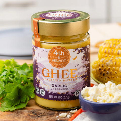 Jar of 4th & Heart Ghee Garlic on a wooden surface with corn and herbs.